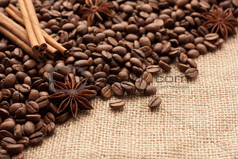 Roasted coffee beans are scattered on sackcloth with star anise and cinnamon sticks.