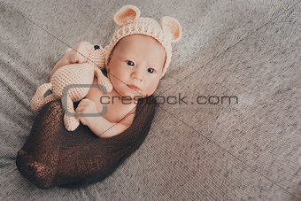 A little child in a beige cap with ears and a knitted beige toy in his hand