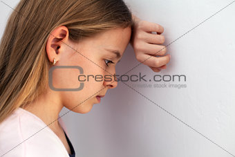 Young sad teenager girl propping her head against the wall