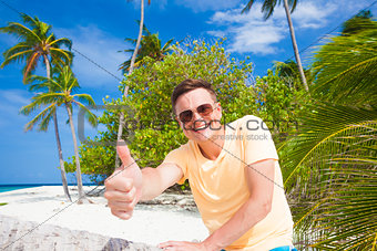 picture of a young man in sunglasses showing thump up at tropical beach