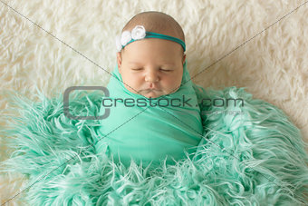 A little child in a greeen diaper lies in a headband with flowers on a beige background. Portrait of newborn