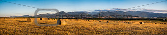 Harvested Field with Hay Bales Under Mountains
