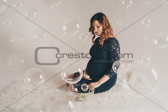 a pregnant woman in a blue dress sitting on the floor. Isolated photo