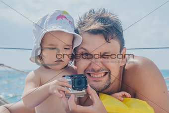 A man takes a little child with a camera in her hands on a lake background.