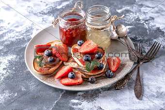 Homemade pancakes with strawberry jam, pieces of fresh strawberries and blueberries